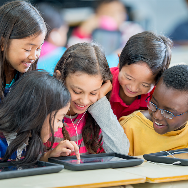 A group of elementary students are having fun, playing an educational game on a tablet.